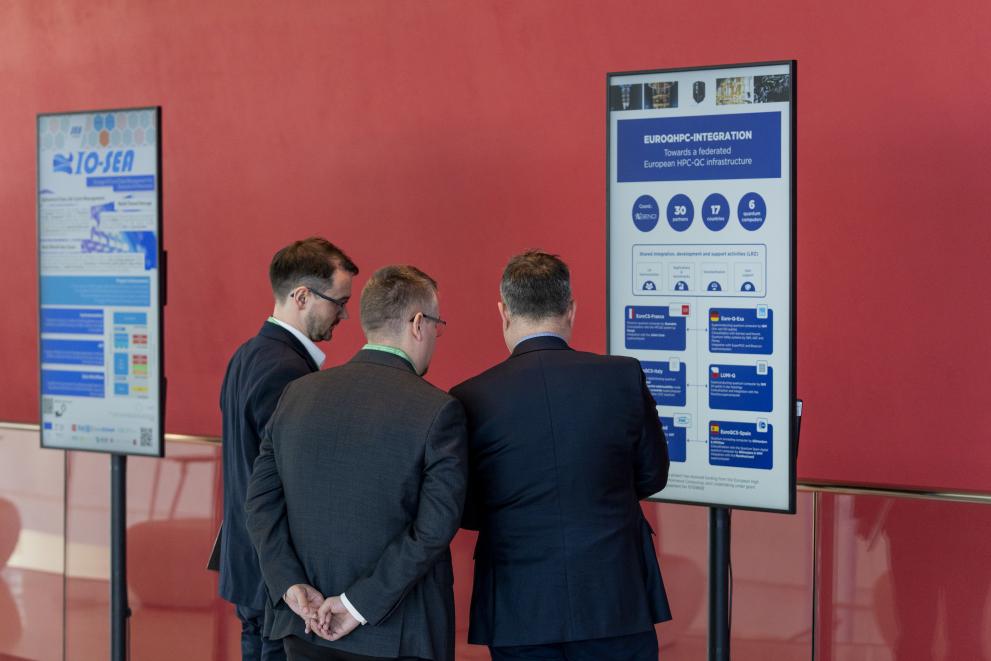 3 men in suits standing and discussion in front of  a poster